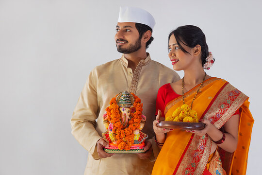 Maharashtrian couple carrying statue of Lord Ganesh and plate of sweet food