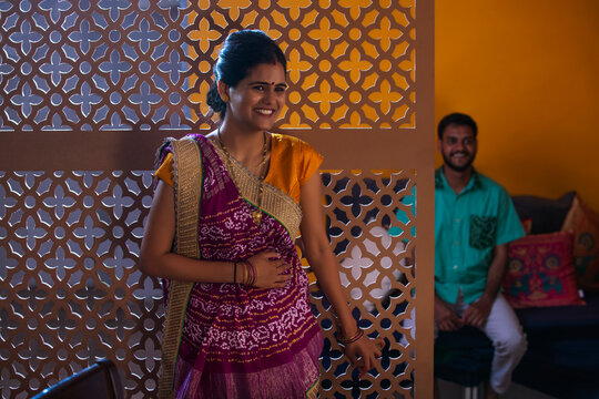 Portrait of smiling Gujrati woman standing and her husband sitting behind