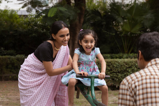 Little girl playing on seesaw with her parent in the park