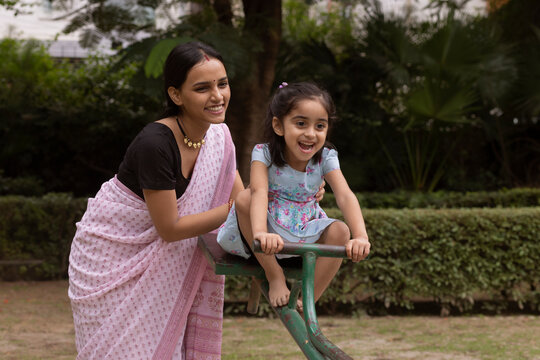Little girl playing on seesaw with her mother in the park