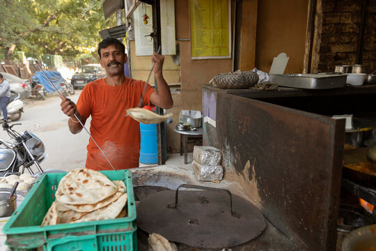 Cook of a local roadside restaurant or a dhaba, making bread or a roti,in a clay wood fired oven or a  tandoor  