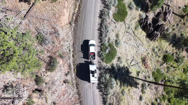 Overhead drone footage captures a pickup truck pulling a travel trailer along a remote forest service road through Modoc National Forest, California.