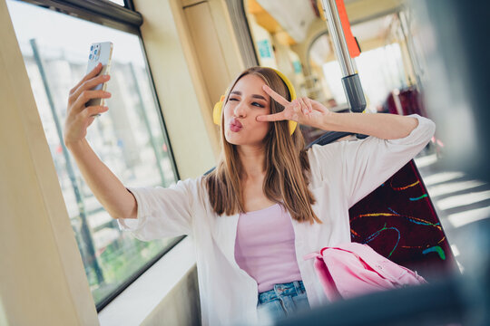 Portrait of nice young student girl smart phone selfie v-sign headphones travel commute public bus transport