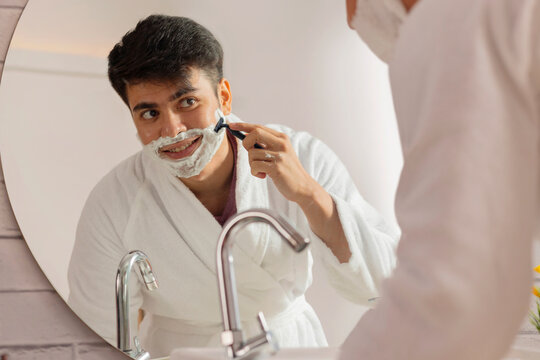 Young man shaving in front of bathroom mirror