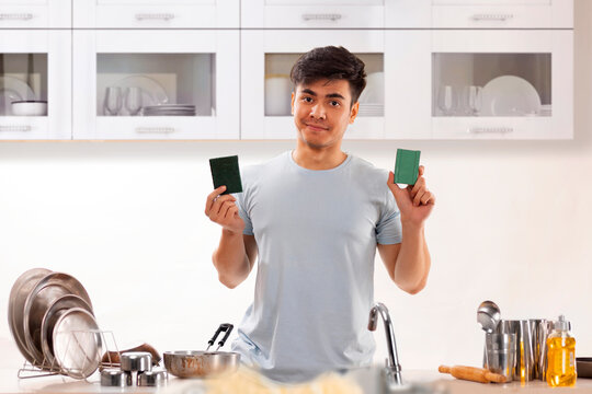 Young man holding dish wash bar and scrub pad in kitchen