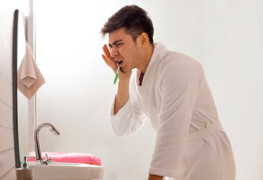 Young man suffering from toothache while brushing