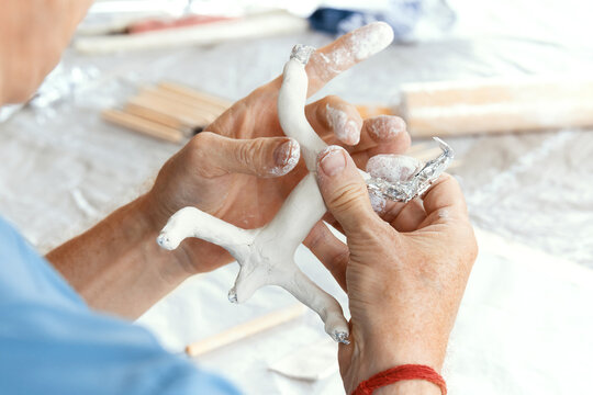 Male hands sculpting clay figure at table with tools in art studio. Creative handmade pottery, workshop and hobby concept.