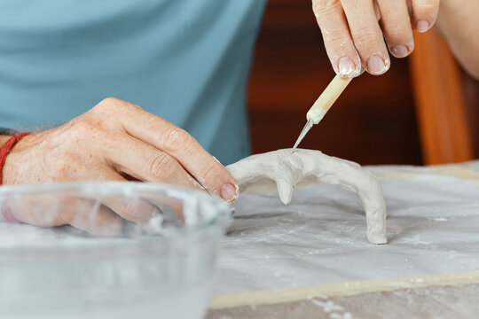 Male hands sculpting clay figure at table with tools in art studio. Creative handmade pottery, workshop and hobby concept.