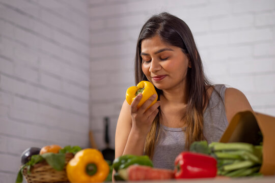 Woman holding a fresh yellow bell pepper in kitchen