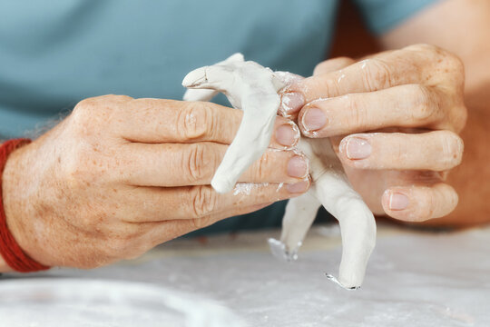 Male hands sculpting clay figure at table with tools in art studio. Creative handmade pottery, workshop and hobby concept.