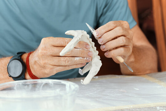 Male hands sculpting clay figure at table with tools in art studio. Creative handmade pottery, workshop and hobby concept.