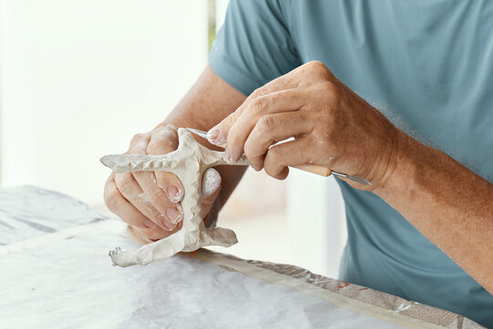 Male hands sculpting clay figure at table with tools in art studio. Creative handmade pottery, workshop and hobby concept.