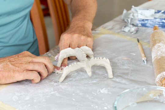 Male hands sculpting clay figure at table with tools in art studio. Creative handmade pottery, workshop and hobby concept.