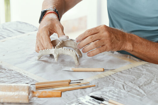 Male hands sculpting clay figure at table with tools in art studio. Creative handmade pottery, workshop and hobby concept.