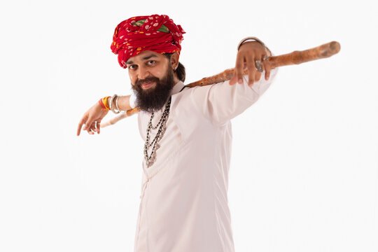 Portrait of Rajasthani man with stick on shoulder standing against white background