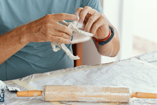 Close up of male hands sculpting clay figure at table. Handmade pottery, creative workshop and ceramics hobby concept.