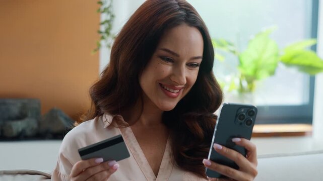 Happy Caucasian woman shopping with mobile phone bank app kissing credit card enjoying spending money online loan approved female girl smiling buying with smartphone order vacation tickets at home