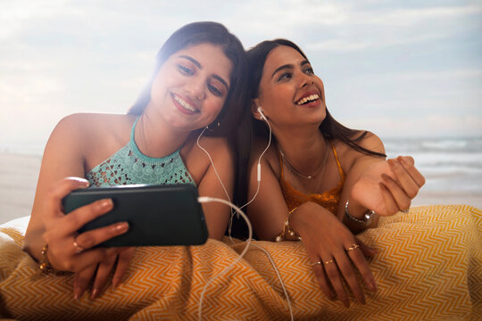 Two female friends listening to music while lying down on beach