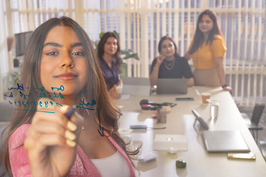 Businesswoman writing on glass while giving business presentation in conference room�