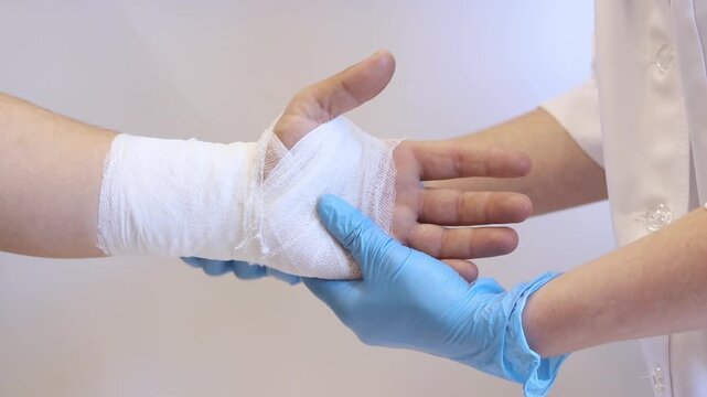 A medical worker in blue gloves applies a sterile gauze bandage to a patient's wrist. First aid for an injury. Close-up of the process of bandaging a hand in a medical institution. Healthcare concept