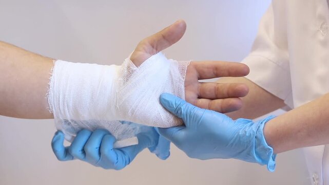 Close-up of the process of bandaging a hand in a medical institution. A doctor carefully bandages a person's wrist with a gauze bandage. Healthcare, traumatology and patient care concept