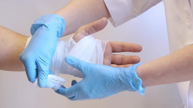 Close-up of the process of bandaging a hand in a medical institution. A doctor carefully bandages a person's wrist with a gauze bandage. Healthcare, traumatology and patient care concept