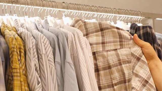 Man chooses male shirt hanging on hanger in store, side view