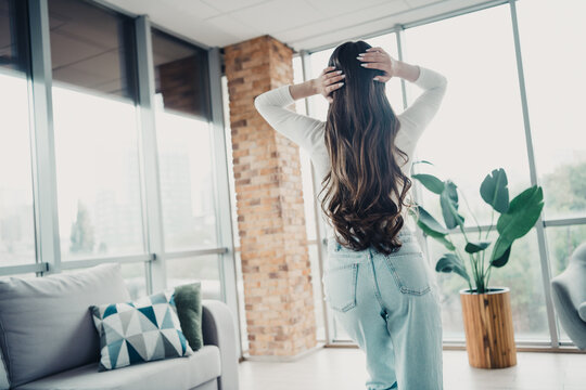 Woman with long hair stretching in a bright apartment by floor-to-ceiling windows in casual jeans and a white top enjoying a relaxed morning lifestyle in a modern living room