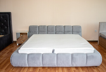 Obraz premium Modern king size double bed with white mattress and quilted grey velvet frame displayed in a furniture showroom interior front view.