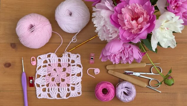 Crochet square lace doily from cotton and acrylic yarn. Bouquet of pink fresh peonies on wooden table. Needlework as a hobby concept. Flat lay, top view, close-up, video