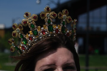 Close up portrait of woman wearing ornate gold crown decorated with green and red jewels on sunny day. © Максим Новосветлов