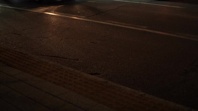 Side view Video of evening city street with paved road, cars in lanes separated by markings. Sidewalk is equipped with raised lines to assist visually impaired or blind pedestrians with orientation