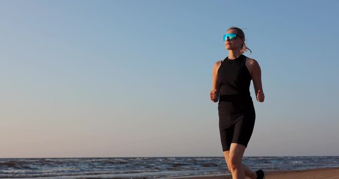 Sporty woman running on beach at sunset in black sportswear. Healthy lifestyle and fitness. Cardio workout