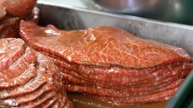 The professional preparation of high quality wagyu beef steaks involves coating thin meat slices in a savory brown marinade within a stainless steel tray for uniform flavor and texture distribution