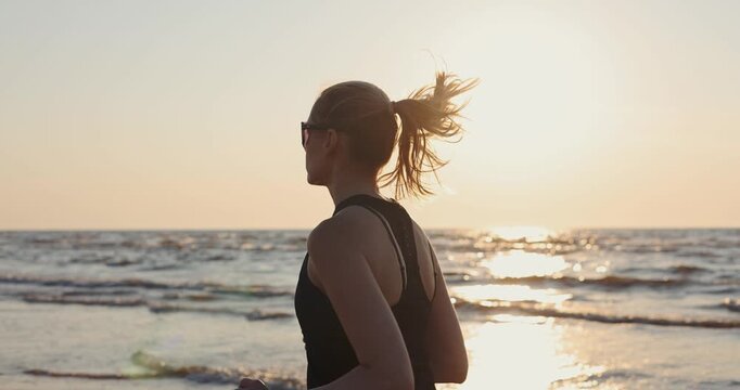 Athletic woman running on beach at sunset in black sportswear. Healthy lifestyle and fitness. Cardio workout