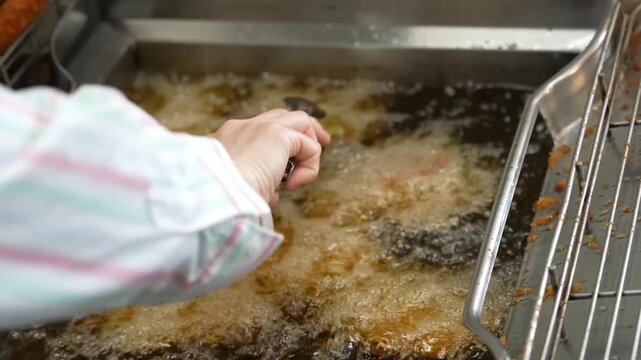 A chef uses culinary tongs to remove hot golden breaded meat skewers from a commercial deep fryer and places the crispy cooked items onto a metal wire rack to drain excess oil for quality service