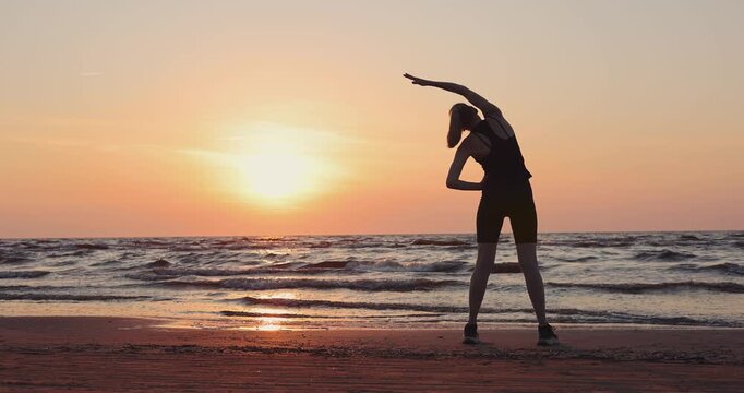 Woman stretching on the beach at sunset. Outdoor fitness and wellness