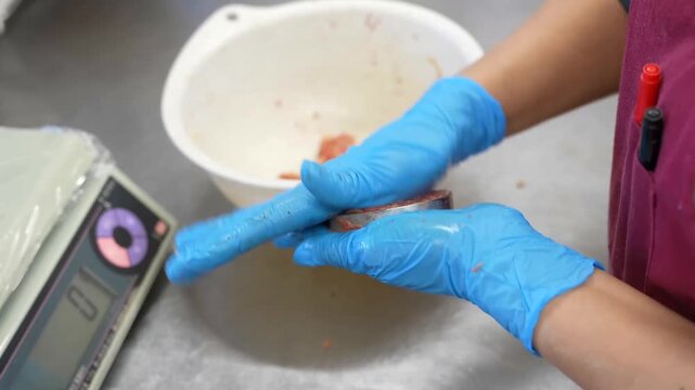 A culinary specialist uses a precision mold to form ground meat patties and coats them in batter and breadcrumbs for cooking in a commercial kitchen food production workspace environment