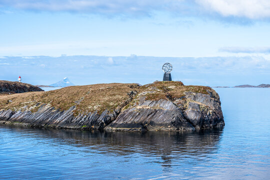 Monument marks the Arctic Circle on Hestmannoy island in Norway with calm sea and distant land in view