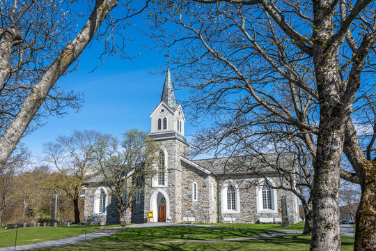 Bronnoysund Church stands in the town of Bronnoysund, Norway, surrounded by trees and blue sky, serving the local community and hosting various church activities