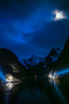 The entrance to Trollfjord in Norway, seen from the water and illuminated by large searchlights at midnight
