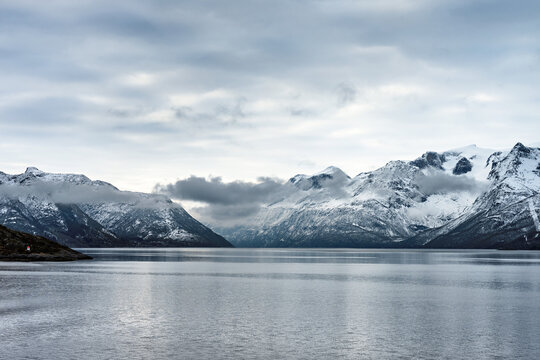 Snowy mountains rise over a still fjord in Norway, showcasing the beauty of Scandinavian nature in winter