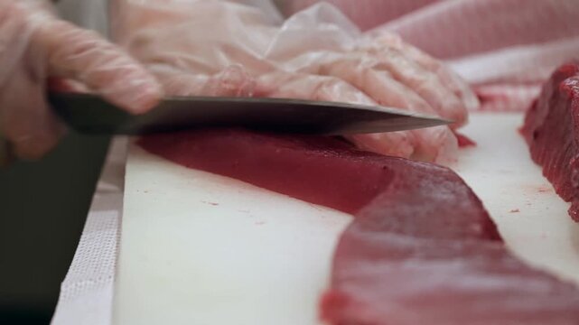 The skilled preparation of raw red tuna on a sterile cutting board utilizes precise knife movements to create uniform sashimi grade portions for high quality culinary service applications