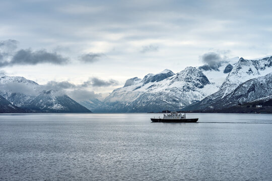 Catch of a ferry in the water surrounded by snowy mountains in Norway during chilly weather