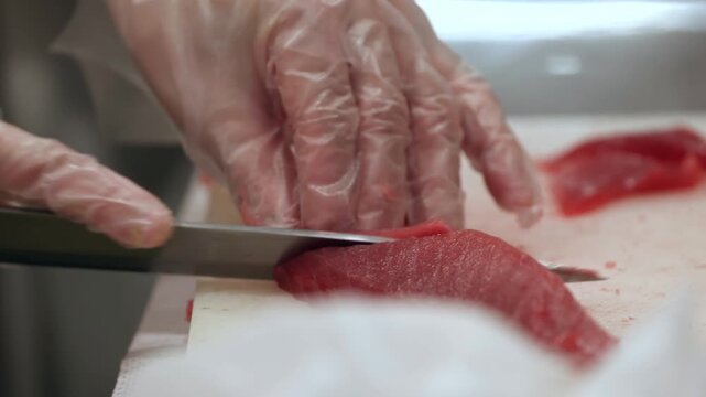The skilled preparation of raw red tuna on a sterile cutting board utilizes precise knife movements to create uniform sashimi grade portions for high quality culinary service applications