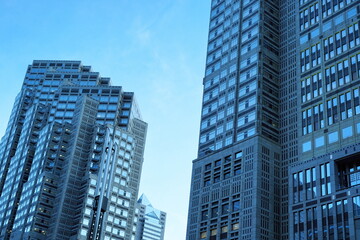 Obraz premium 青空を背景にそびえ立つ複数の高層ビルディング群の景観。現代的な建築デザインとガラス張りの窓が都市のクールで洗練された雰囲気を強調している。未来的な都市景観を表現。