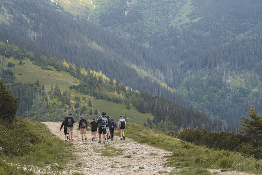 Group of young hikers walking along a dirt trail on a mountain ridge, people trekking through alpine landscape during summer outdoor adventure