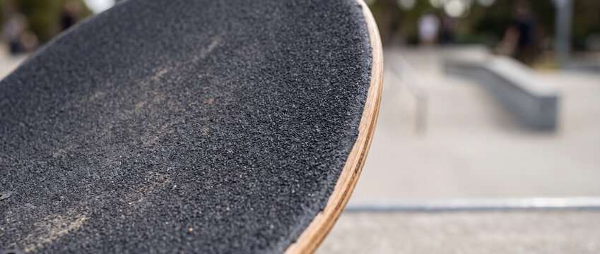 Close-up skateboard grip tape at urban skatepark deck detail with blurred concrete ramps