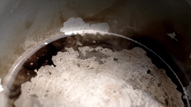 Worn stainless steel interior of a cooking pot with burnt residue and scratches. Abstract industrial texture with natural wear. Rotation