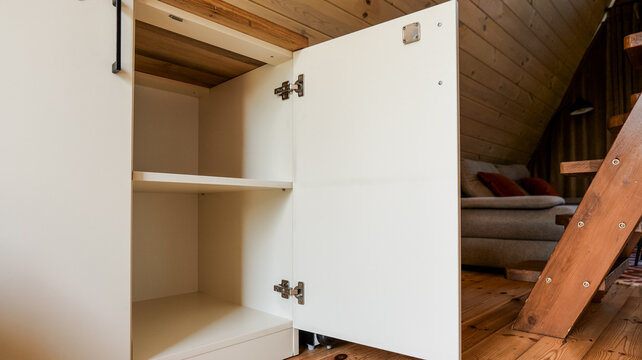 Modern white cabinet with open door revealing empty shelves and wooden interior details